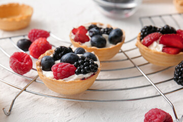 Stand of tasty tartlets with whipped cream and berries on white background