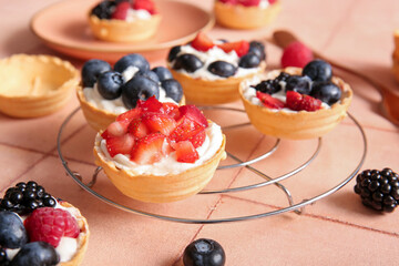 Stand of tasty tartlets with whipped cream and berries on pink tile background