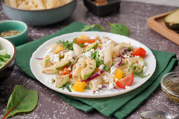 Plate of tasty pasta salad with tomatoes and avocado on dark background