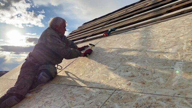 Roofer man on roof making repairs in Ukraine after war damage. Roof renovation and preparation for laying shingles on OSB boards