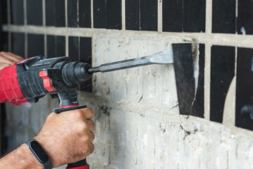 Builder with a puncher dismantles old tiles from a concrete wall