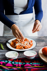 Mexican woman hands preparing chilaquiles with red sauce and eating traditional mexican food for breakfast in Mexico Latin America