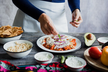 Mexican woman hands preparing chilaquiles with red sauce and eating traditional mexican food for breakfast in Mexico Latin America