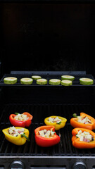 View of grilling stuffed savory bell peppers topped with melted cheese over the fire on an outdoor summer BBQ or picnic