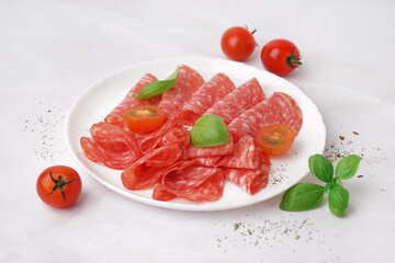 Plate with slices of tasty salami on light background