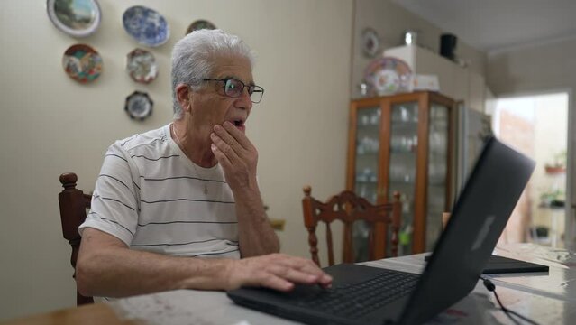 Senior man using laptop at home, casual elderly person engaged with modern technology, browsing internet online looking at computer screen
