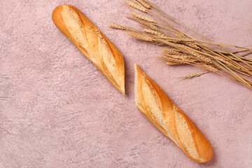 Sliced baguette and wheat ears on pink table