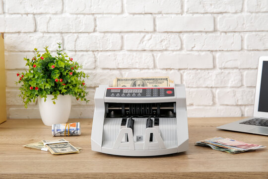 Cash counting machine with dollar banknotes on table in office