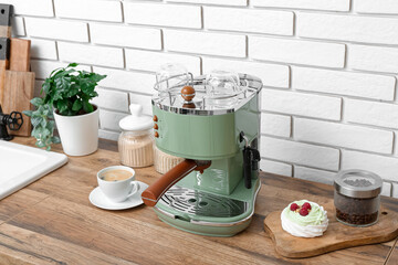 Modern coffee machine with cup of hot espresso and cake on table in kitchen