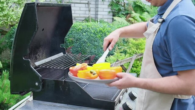 man spreads grilled pepper with tongs. Juicy fresh pepper with egg, tomato cherry and cheese are fried in grill. Cooking delicious vegetarian dish in your home kitchen.