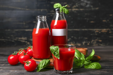Bottles and glass of tasty juice on black wooden background