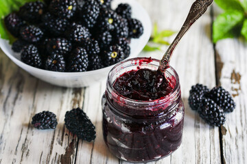 Overhead view of homemade blackberry preserves or jam in a mason jar surrounded by fresh organic blackberries. Selective focus with blurred foreground and background.