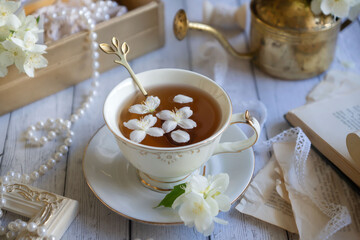Cup of aromatic jasmine tea and fresh flowers on wooden table, flat lay