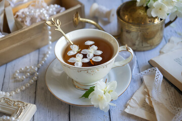 Cup of aromatic jasmine tea and fresh flowers on wooden table, flat lay