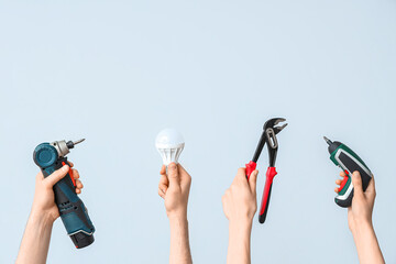 Electrician hands with light bulb and tools on grey background