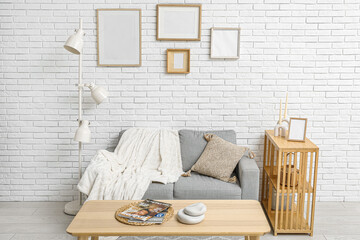 Interior of stylish living room with sofa and blank frames on white brick wall