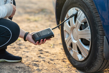 A woman's hand holds a wireless portable air pump for inflating car tires