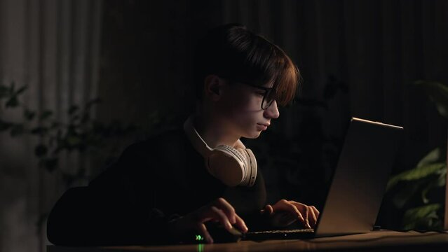 Video games gambling addiction. Concentrated teen boy plays a computer shooter video game, esport, virtual competition on mouse with keyboard at dark home room. Online video game technology concept
