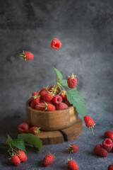 Fototapeta na wymiar Ripe, sweet raspberries falling into a plate on a dark background.