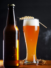 Tall glass of wheat beer and beer bottle on wooden table with dark background