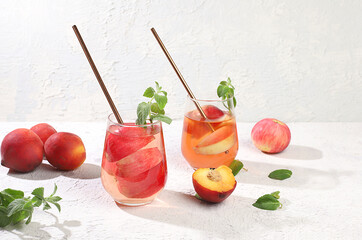 Iced peach tea or cocktail with mint and lobdom,recipe for refreshing summer drink.Two glasses with peach fruit lemonade on light concrete table,detox diet and weight loss concept,menu for restaurant