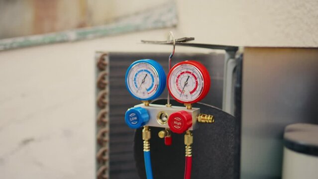 Dolly in close up of yellow safety helmet and manifold gauges used for checking air conditioner freon in need of maintenance. Set of refrigerant levels benchmarking tool mounted on condenser