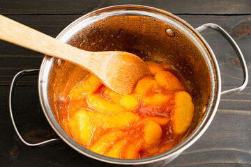 Spiced Peaches and Sugar Cooked in a Small Pan: Making peach syrup in a small saucepan with a wooden spoon