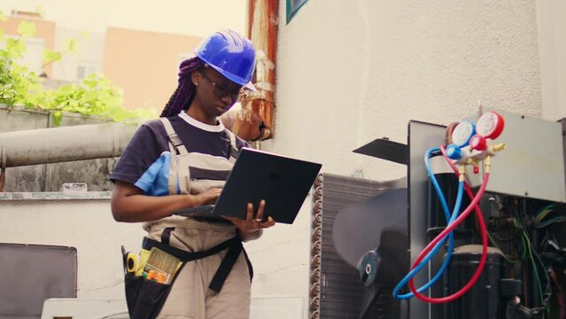Certified technician working on outdoor hvac system, holding laptop. Competent mechanic optimizing external air conditioner performance, ensuring it operates at maximum capacity