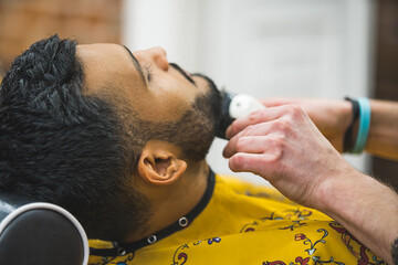 Side view face of a young man in the barbershop - Barber trimming beard using trimmer. High quality photo