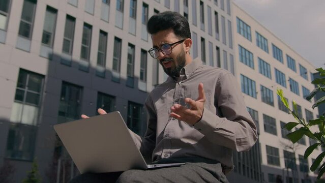 Arabian Indian businessman working on laptop in city outdoors worried man anxious male executive manager ceo have computer problem difficulties loss failure low battery error rejected business project