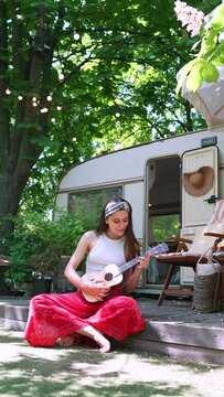  beautiful hippie girl is singing a song and playing the guitar near the trailer