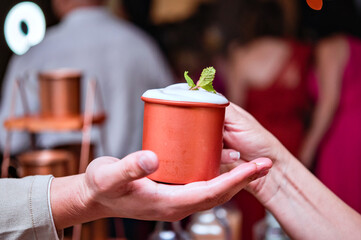A copper cup with a moscow mule being handed by one hand to another hand