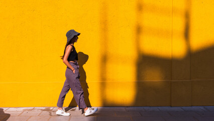 dark-haired girl in hat while walking. as background an orange wall