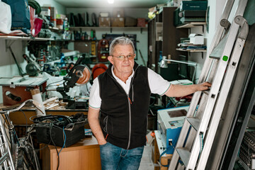 Portrait of smiling positive senior male standing in workshop with tools and equipment