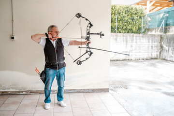 Elderly senior archer shooting bow. Mature man training preparing bow and arrow for sport copy space