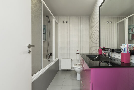A bathroom with a glossy black sink, wood cabinet with deep purple