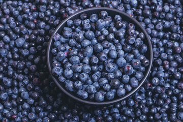 Fresh blueberries in black bowl on blueberries background.  Close-up. Top view. Bowl filled with...