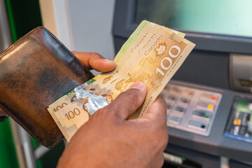 Cash withdrawal at an ATM. Money in the hands of close-up. Canadian dollars banknotes and cash...