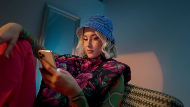 Fashionable young woman sitting on the sofa, surfing a on the internet on her mobile phone