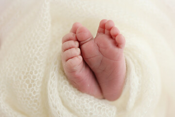 The tiny foot of a newborn baby. Soft feet of a new born in a white wool blanket. Close up of toes, heels and feet of a newborn. Knitted white heart in the legs of a baby. Macro photography.