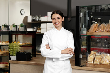 Fototapeta na wymiar Portrait of happy baker near showcase with pastries in her cafe