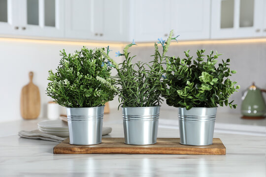 Different artificial potted herbs on white marble table in kitchen