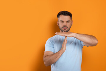 Handsome man showing time out gesture on orange background, space for text. Stop signal