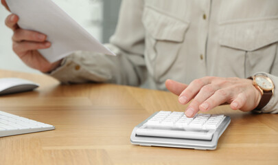 Fototapeta premium Professional accountant using calculator at wooden desk in office, closeup