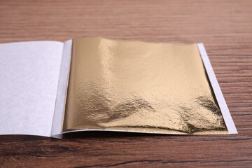 Edible gold leaf sheet on wooden table, closeup