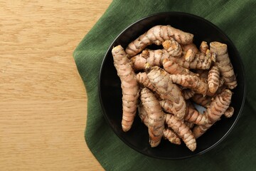 Bowl with raw turmeric roots on wooden table, top view. Space for text