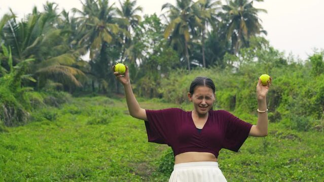 young woman comically juggles tennis balls accidentally hitting one on her head