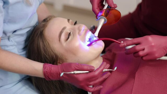 Ultraviolet light, Restoration light, Clinic patient. Stomatologist, in dental clinic room, exposes photopolymer on patient's teeth to ultraviolet light as part of restoration treatment.