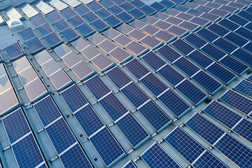 Aerial view of solar power plant with blue photovoltaic panels mounted on industrial building roof for producing green ecological electricity. Production of sustainable energy concept