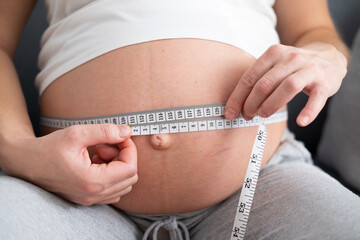 Pregnant girl measures her belly with a measuring tape